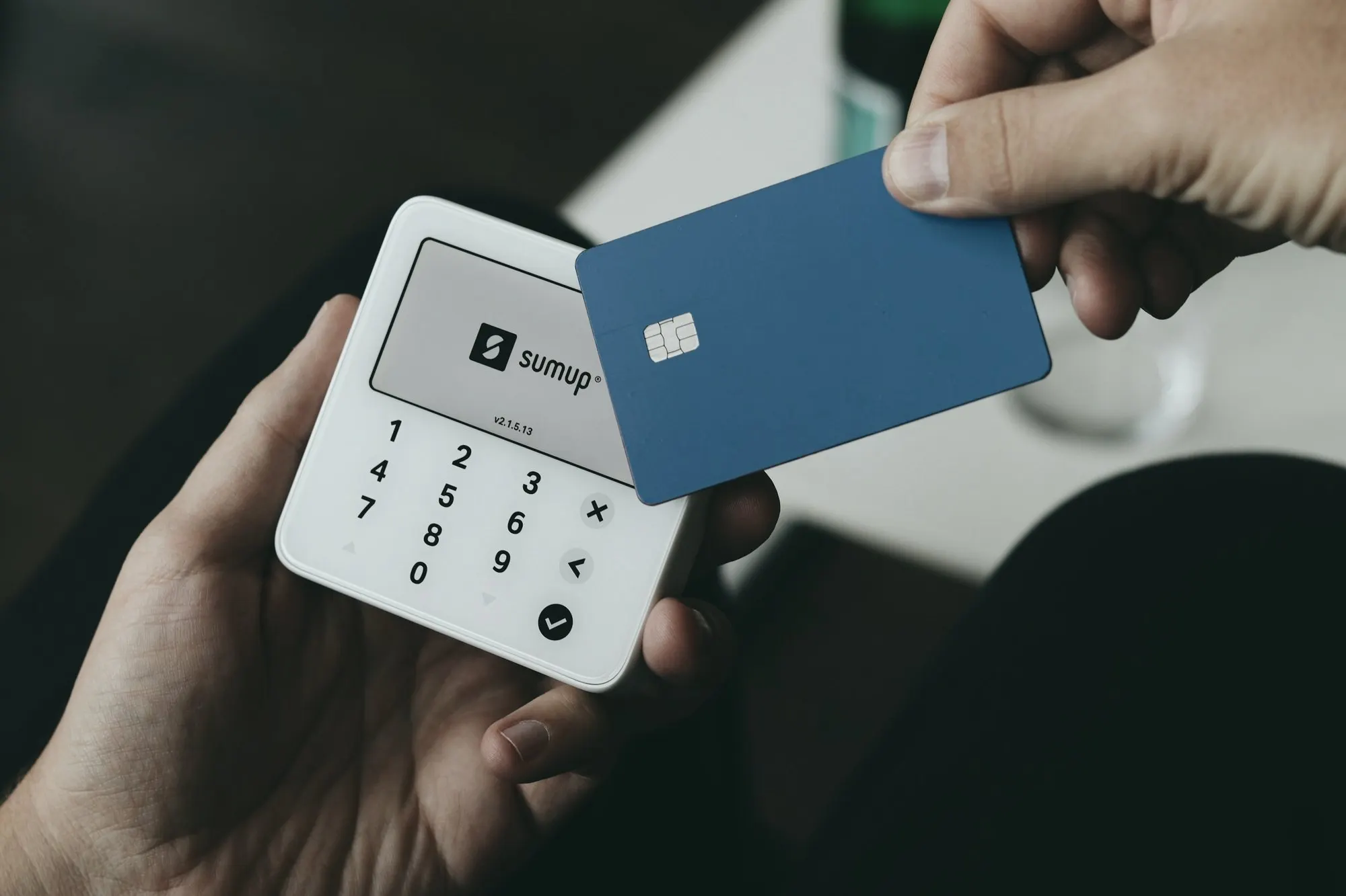 A hand holds a handheld card terminal while another hand inserts a blue chip card.