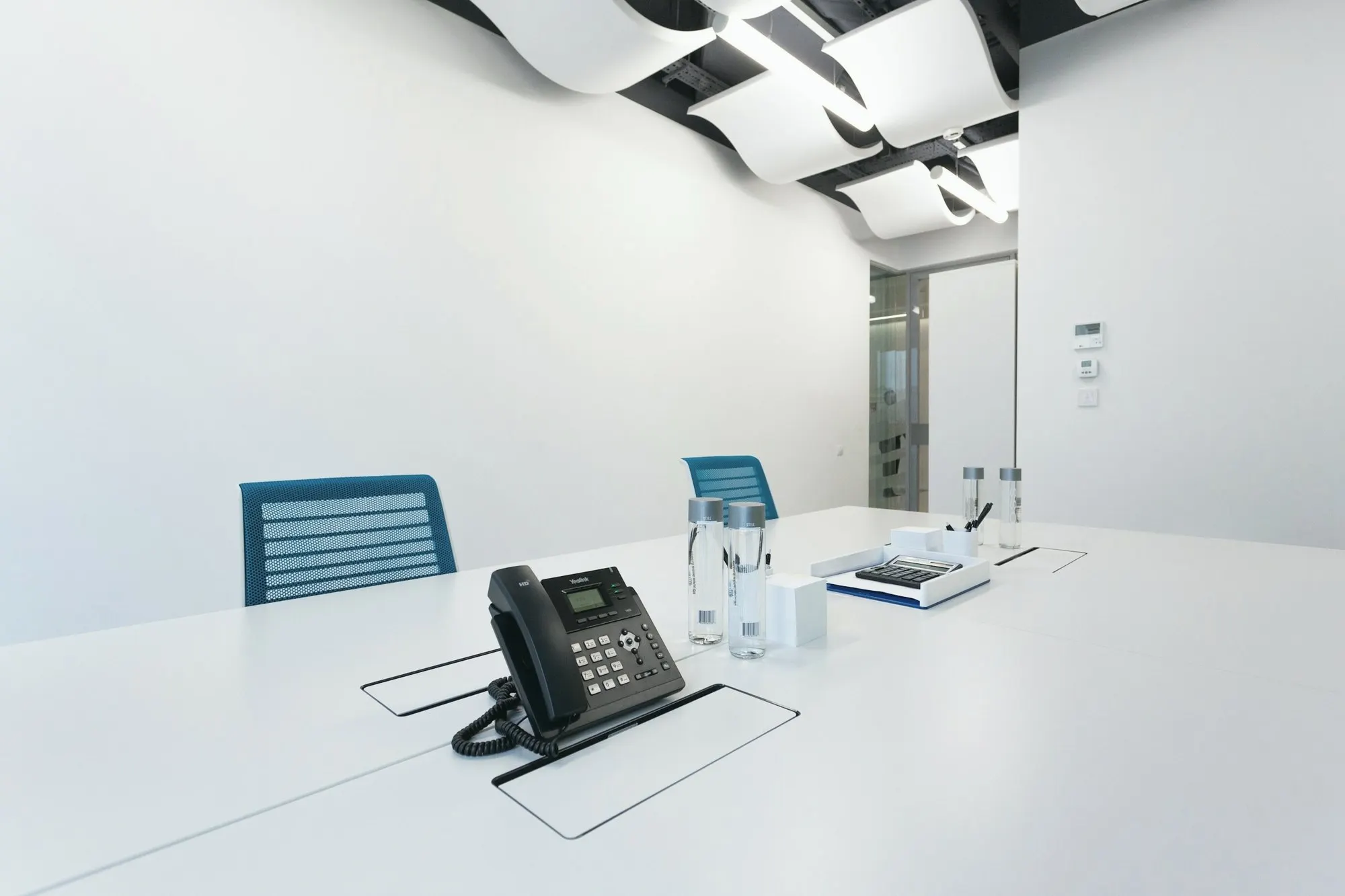 A black desk phone sits on a white conference table in a bright meeting room.