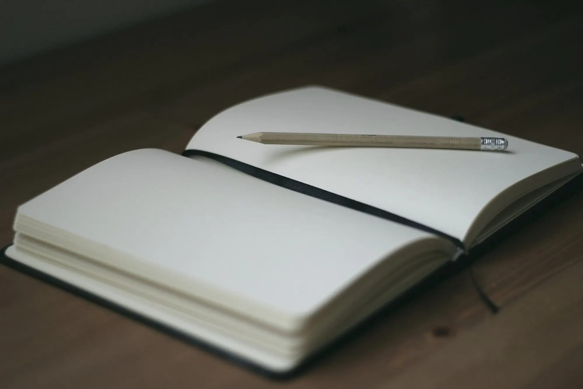 An open blank notebook with a pencil resting on a dark wooden table.