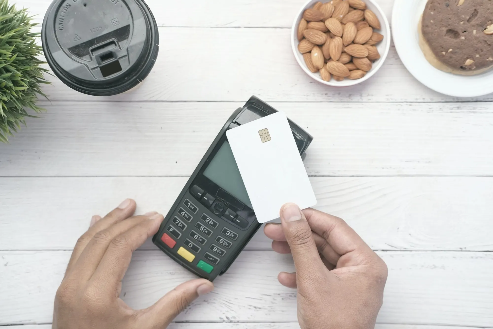 Hands tapping a blank card on a countertop card terminal.