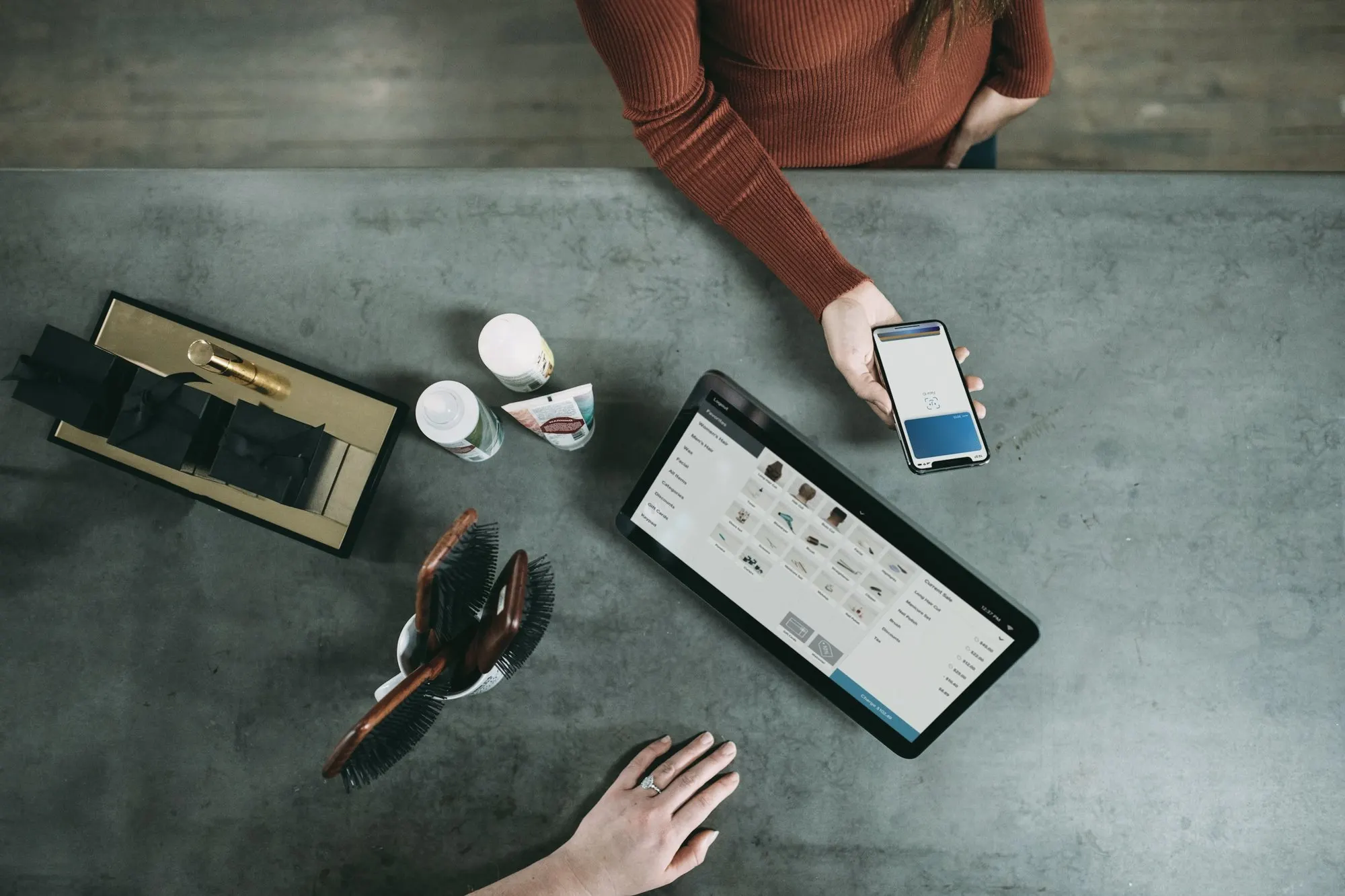 Overhead view of a checkout counter where a customer holds a phone beside a tablet register.