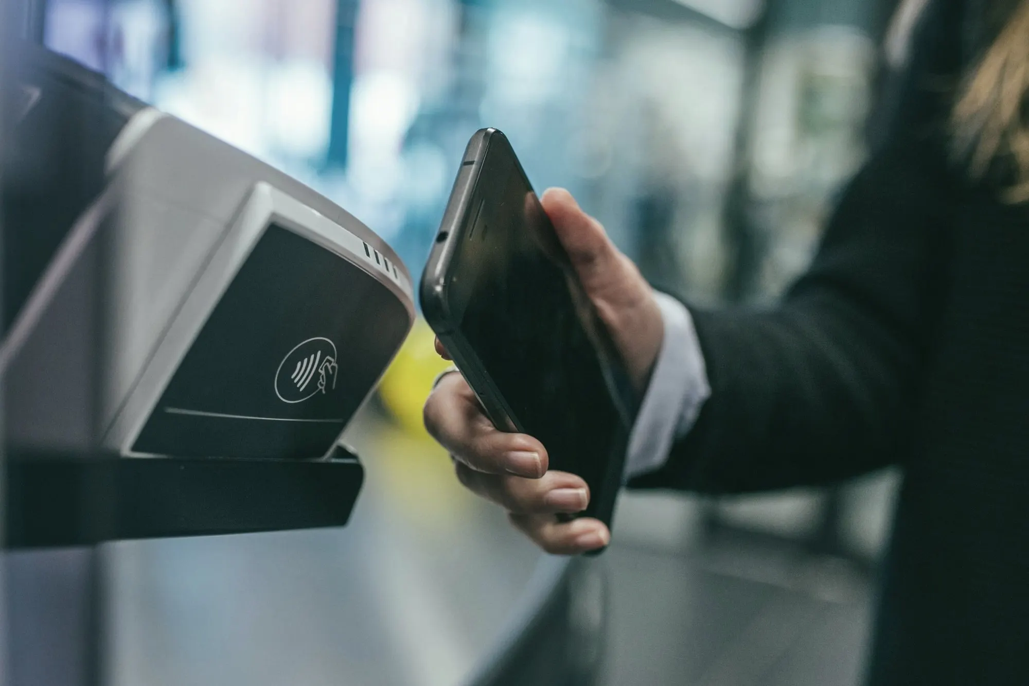 A hand holding a smartphone up to a contactless payment reader.