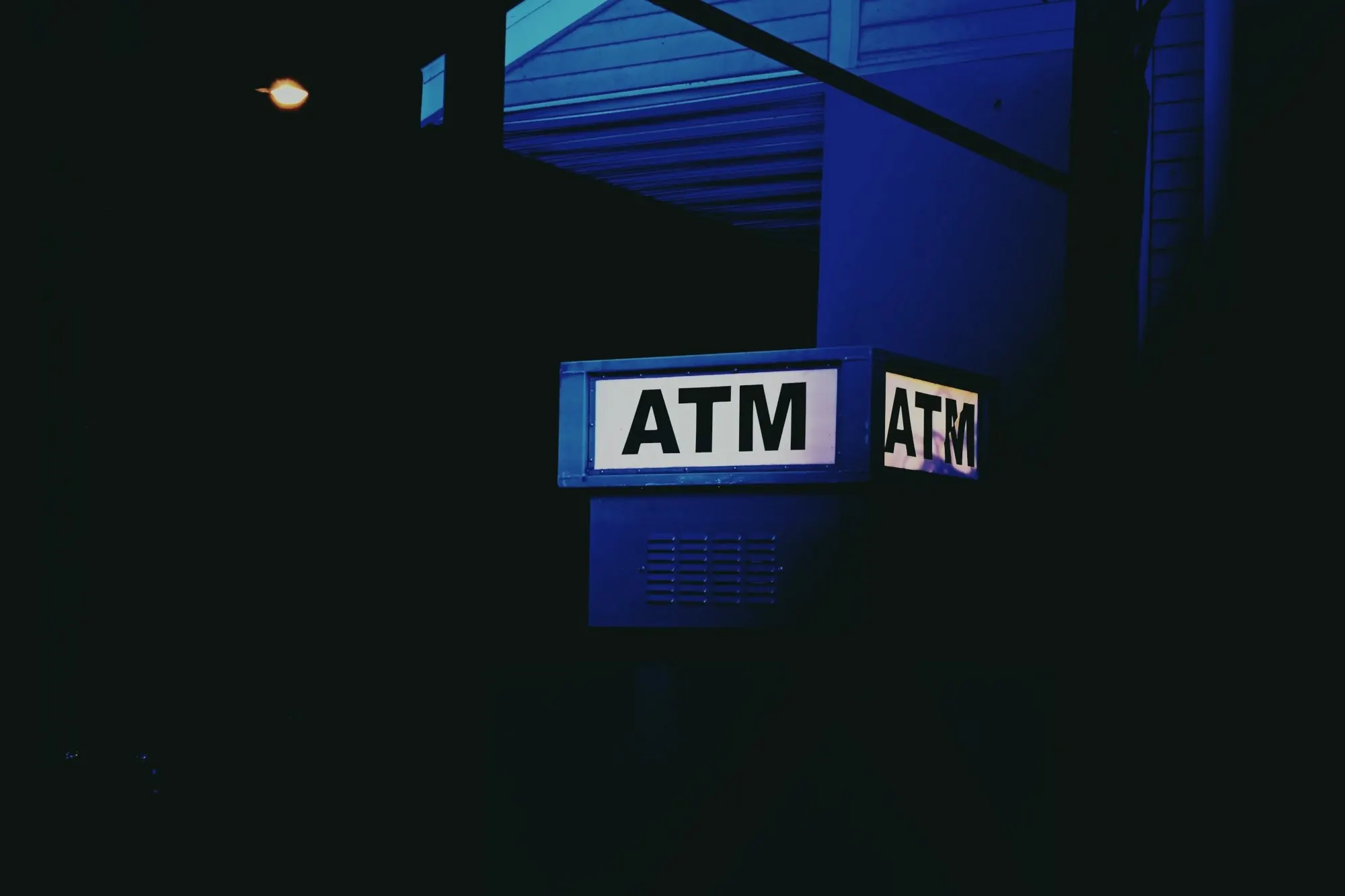 A lit ATM sign glowing on a dark wall at night.