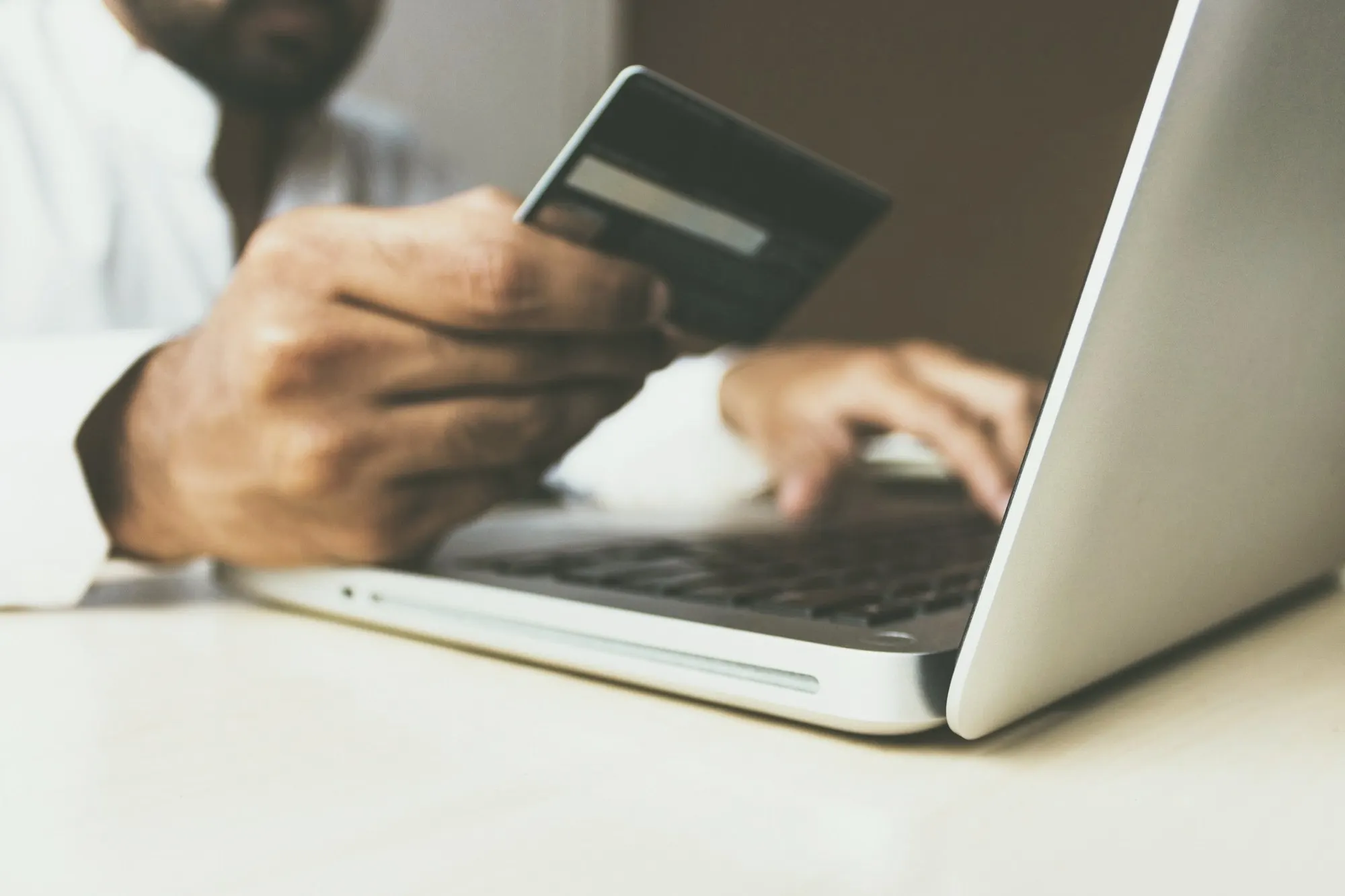 A hand holds a credit card above a laptop keyboard while the other hand types.
