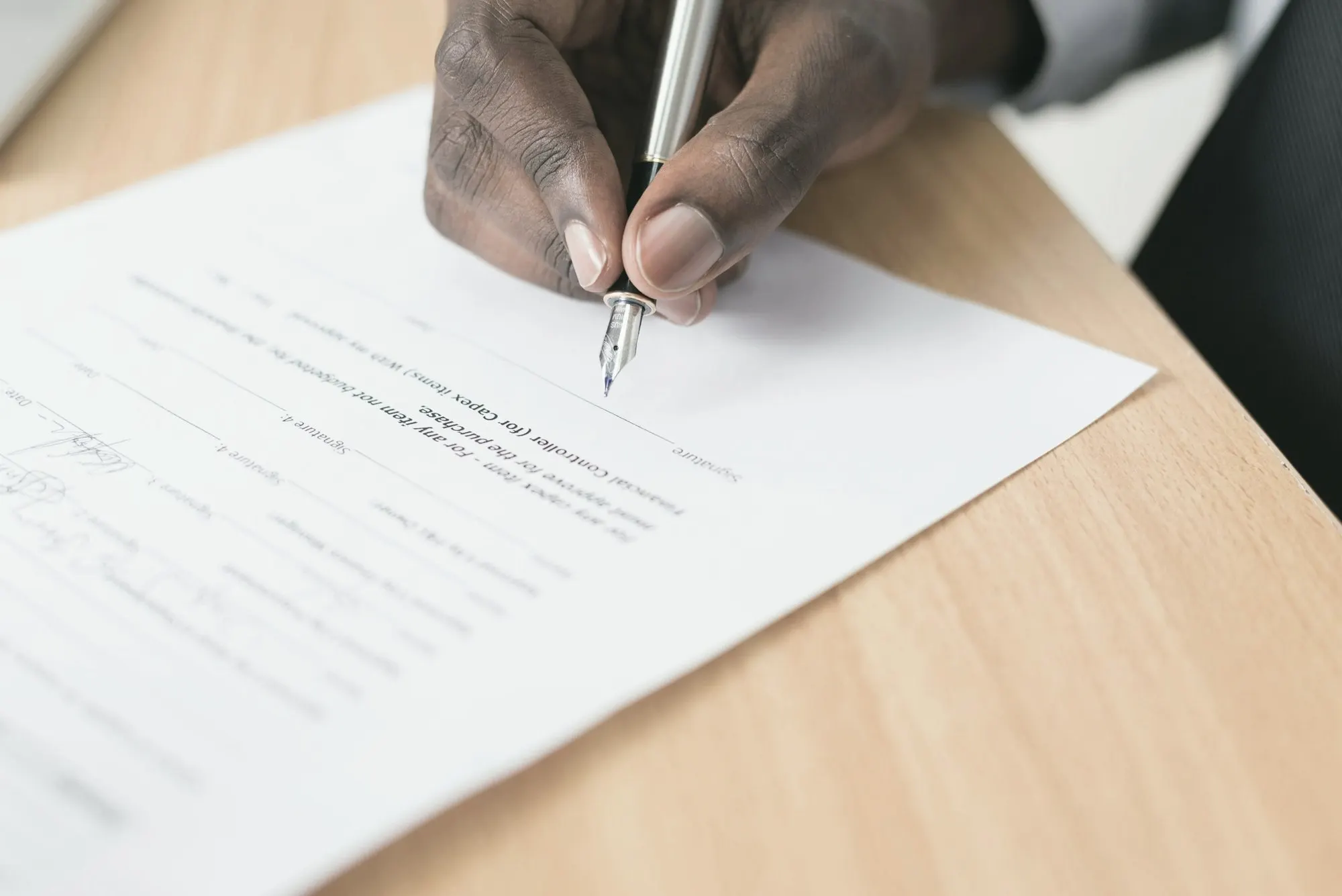A hand writing on a paper form at a desk, like a merchant application.