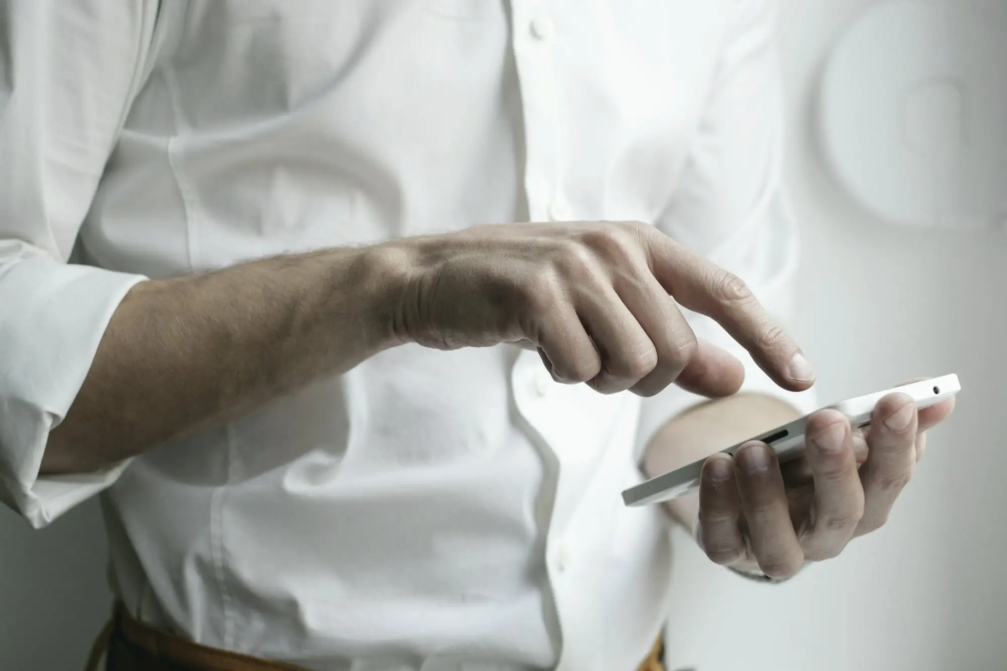 A person in a white shirt taps the screen of a smartphone held in one hand.