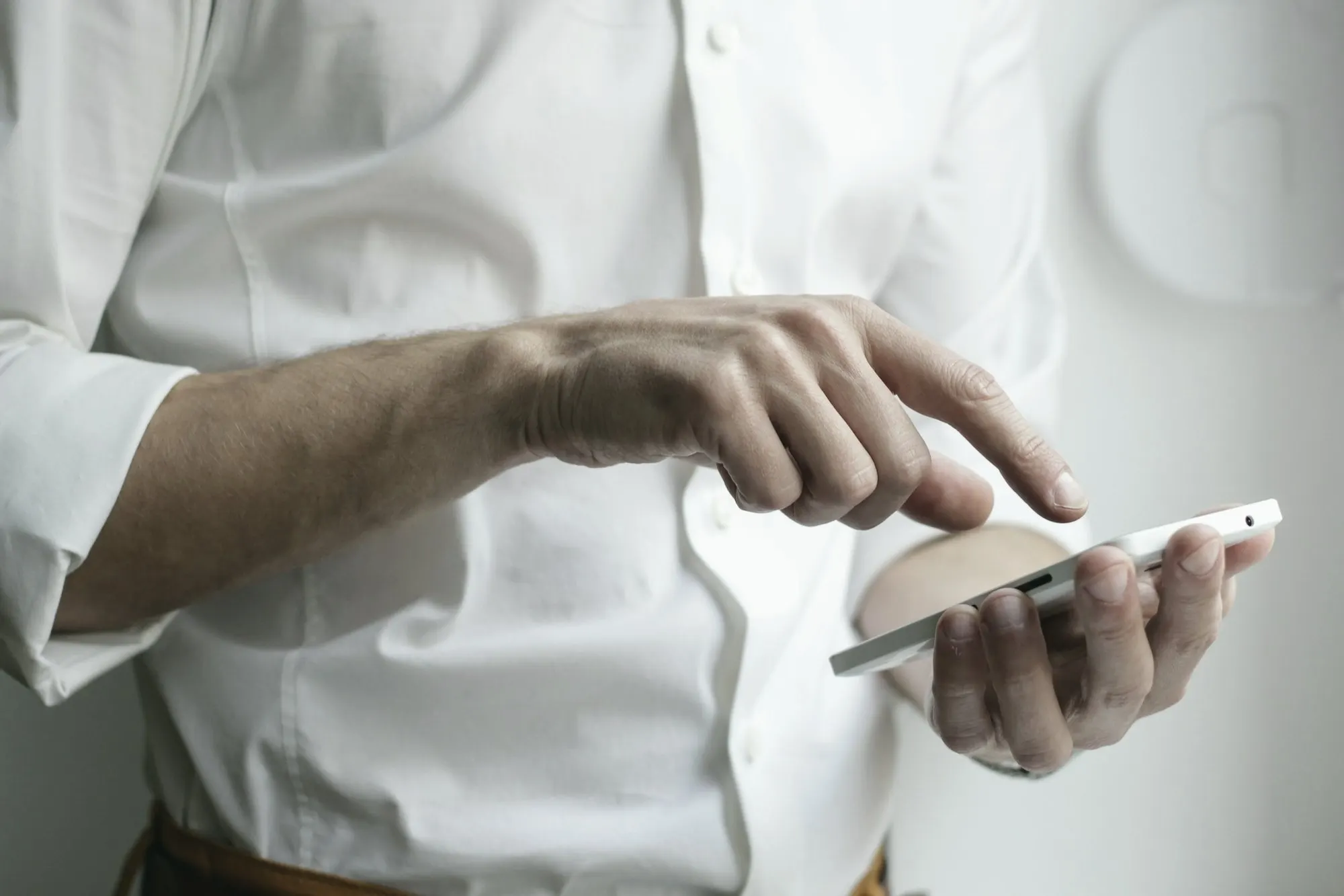 A person in a white shirt taps the screen of a smartphone held in one hand.