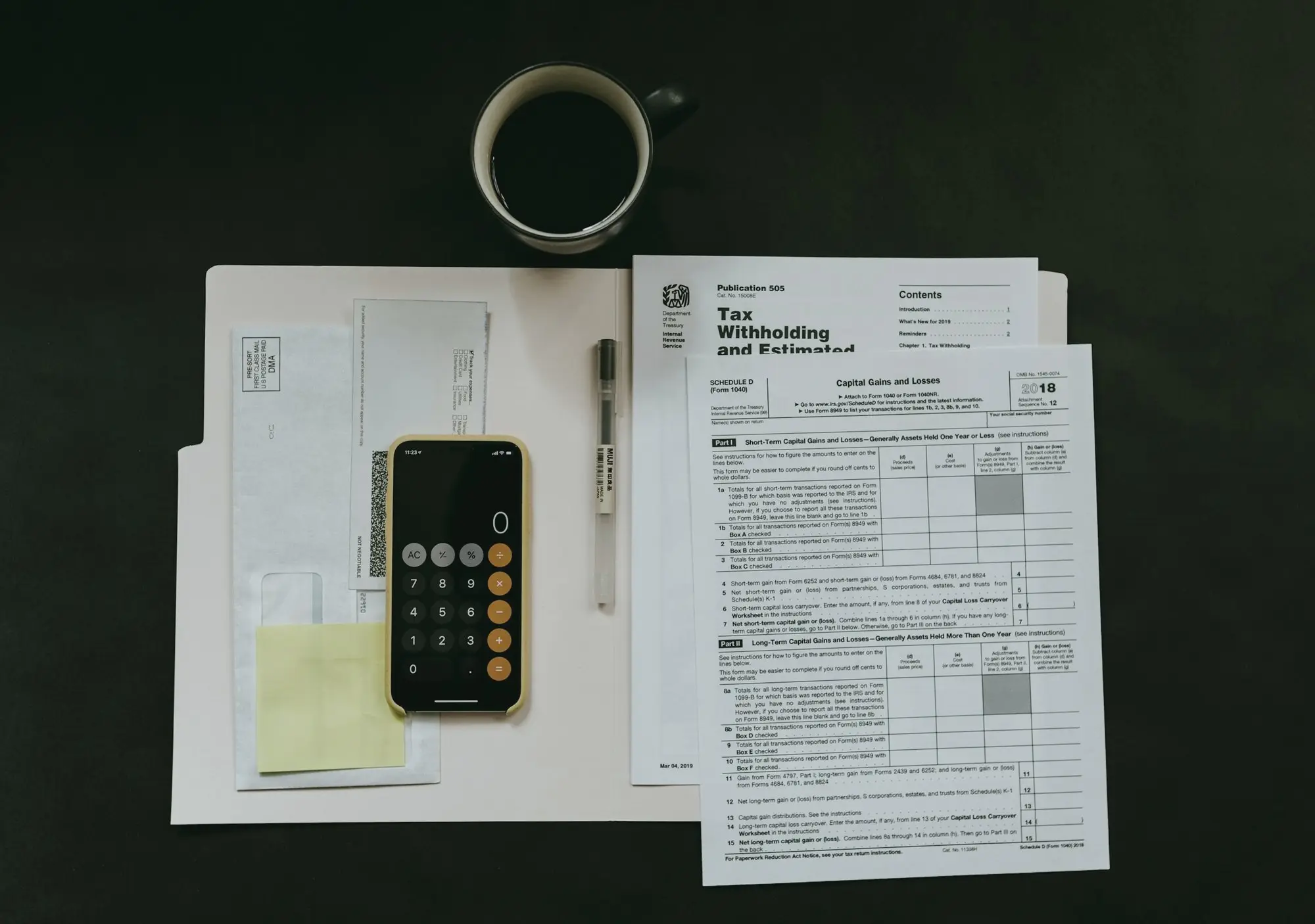 Paper forms, a calculator on a phone, and a pen laid out beside a coffee cup.