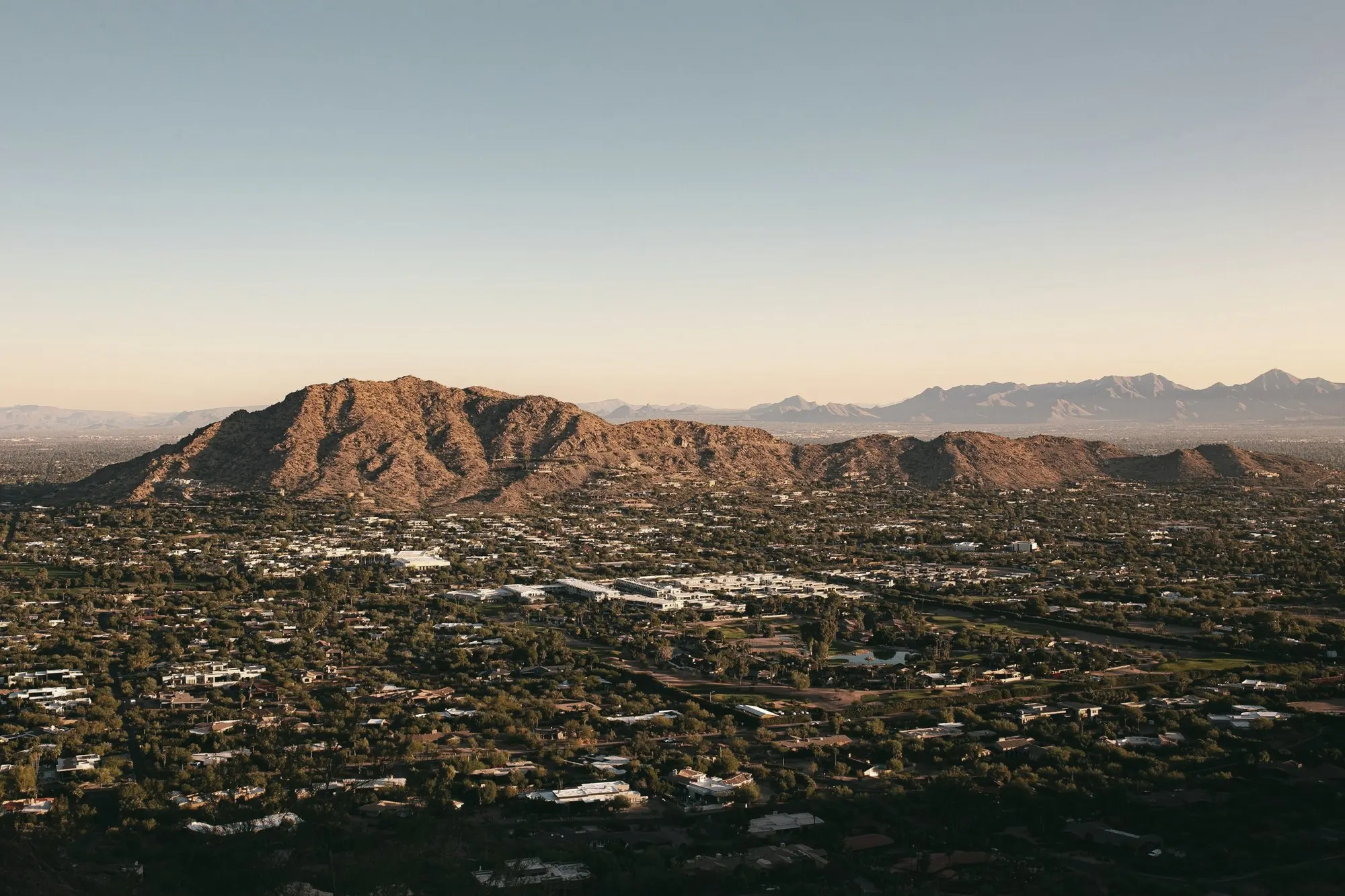 Phoenix-area neighborhoods spread below a desert mountain at golden hour