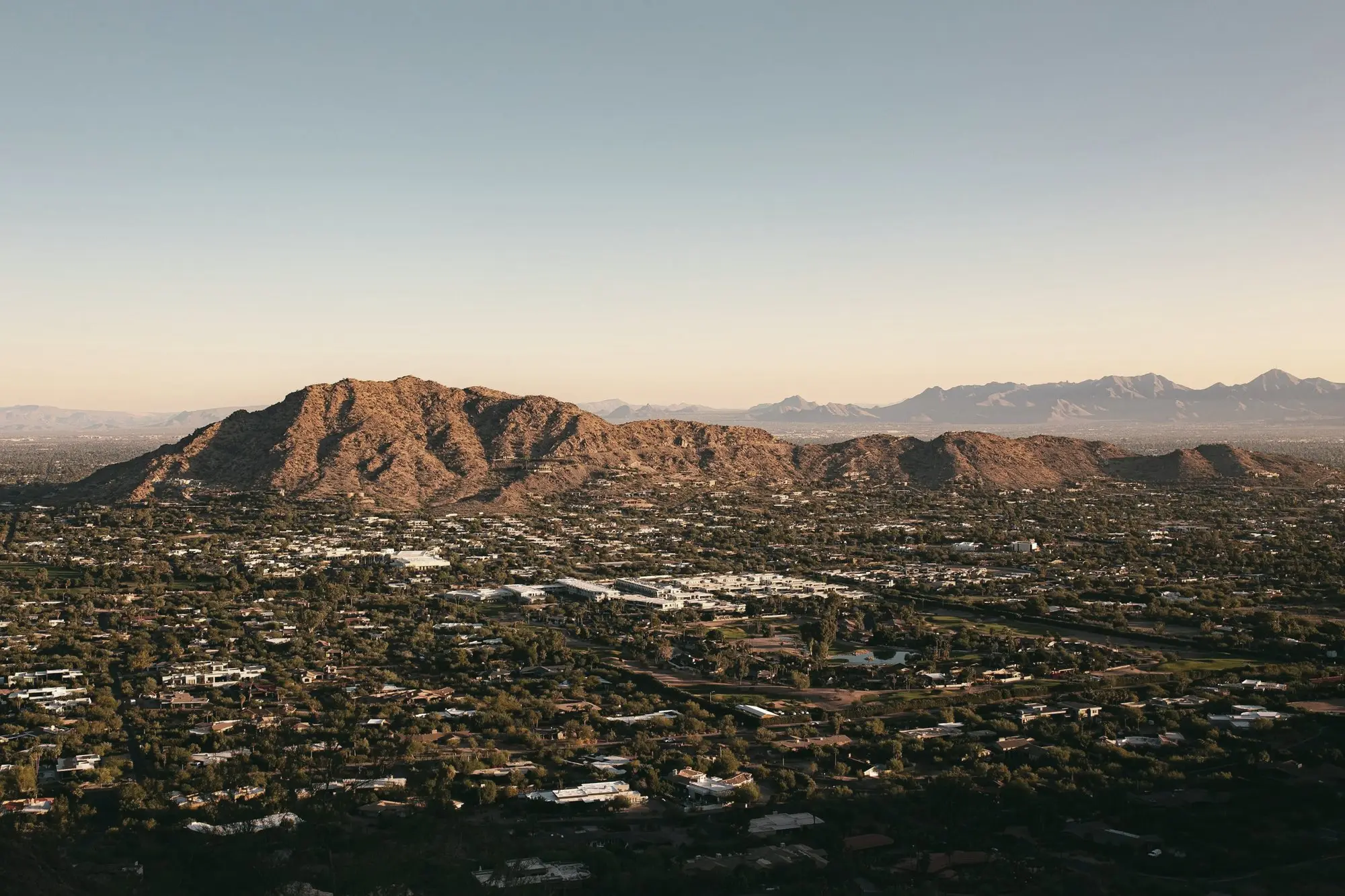 Phoenix-area neighborhoods spread below a desert mountain at golden hour